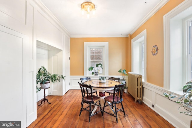 dining space with crown molding, a decorative wall, hardwood / wood-style flooring, and radiator