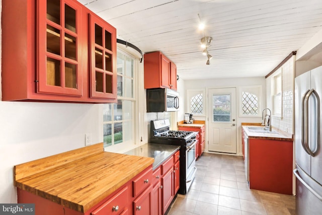 kitchen featuring glass insert cabinets, a sink, stainless steel appliances, track lighting, and light tile patterned flooring