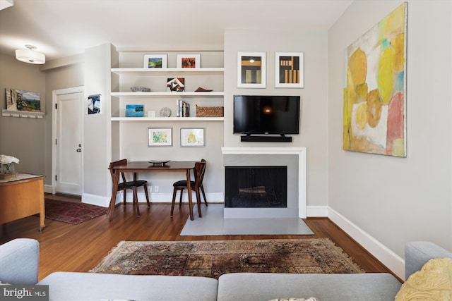 living area with dark wood-type flooring, a fireplace with flush hearth, and baseboards