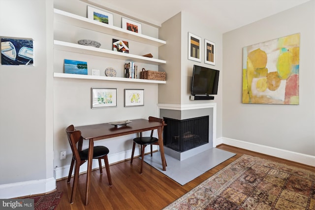 office space with baseboards, dark wood-type flooring, and a multi sided fireplace