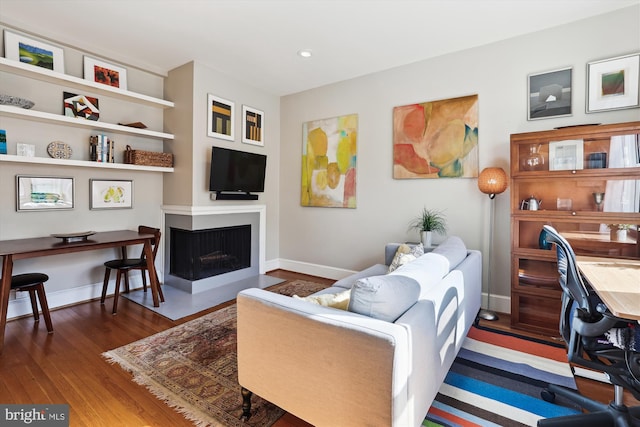 living room featuring a fireplace with flush hearth, dark wood finished floors, and baseboards