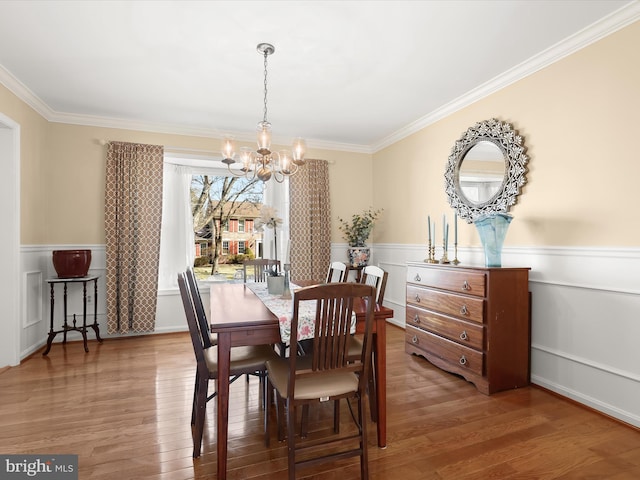 dining room with wood finished floors, crown molding, a wainscoted wall, and an inviting chandelier