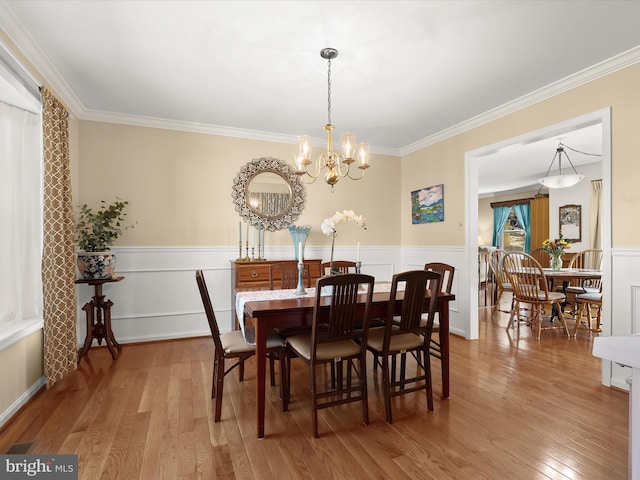dining room with wainscoting, crown molding, a chandelier, and light wood finished floors