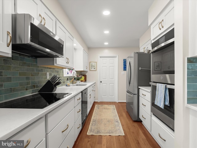 kitchen featuring backsplash, wood finished floors, a sink, appliances with stainless steel finishes, and white cabinetry