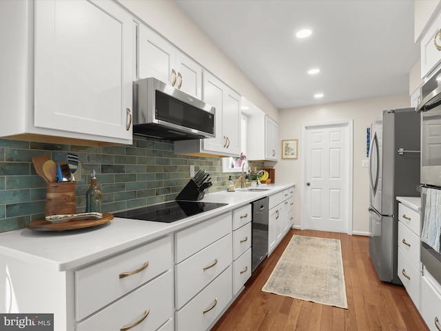 kitchen featuring wood finished floors, a sink, white cabinetry, and appliances with stainless steel finishes