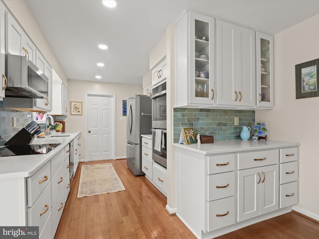 kitchen with white cabinets, backsplash, appliances with stainless steel finishes, and light wood-style floors