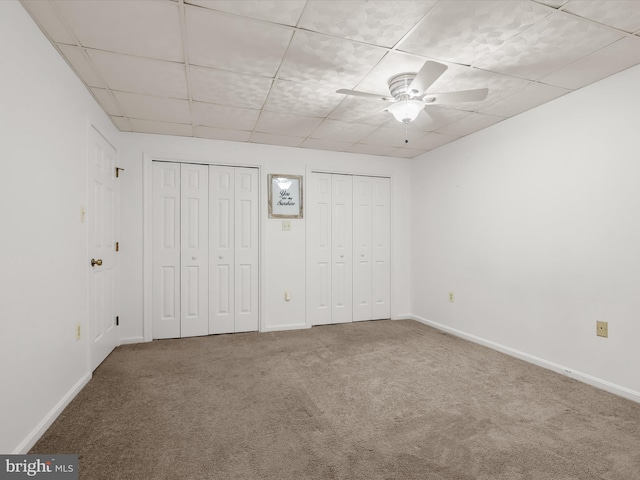 unfurnished bedroom with baseboards, multiple closets, a drop ceiling, and carpet