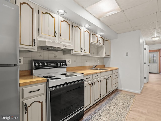 kitchen featuring a sink, tasteful backsplash, electric range, freestanding refrigerator, and under cabinet range hood