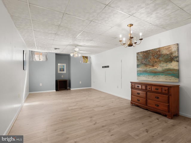 basement featuring baseboards, a drop ceiling, light wood finished floors, and ceiling fan with notable chandelier