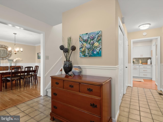 hallway with light tile patterned flooring, crown molding, and an inviting chandelier