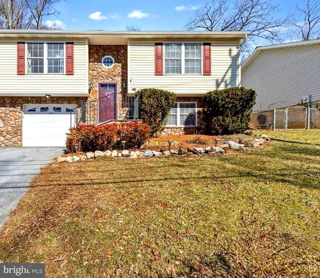 bi-level home with aphalt driveway, a garage, fence, stone siding, and a front yard