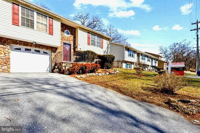 split foyer home with aphalt driveway, stone siding, and an attached garage