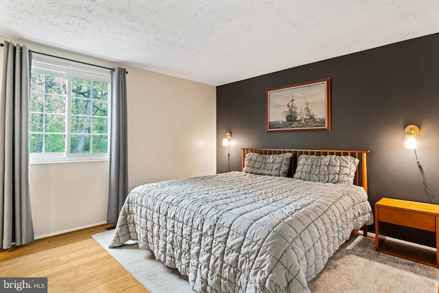 bedroom featuring an accent wall, baseboards, wood finished floors, and a textured ceiling