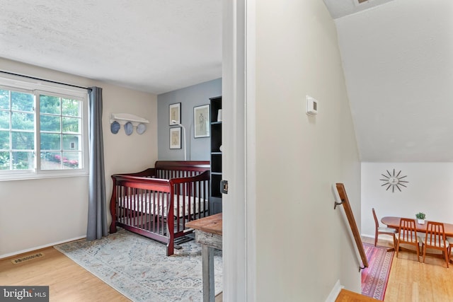 bedroom with a nursery area, baseboards, wood finished floors, and visible vents