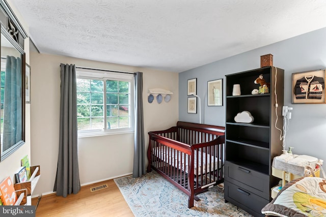 bedroom featuring baseboards, wood finished floors, visible vents, and a textured ceiling