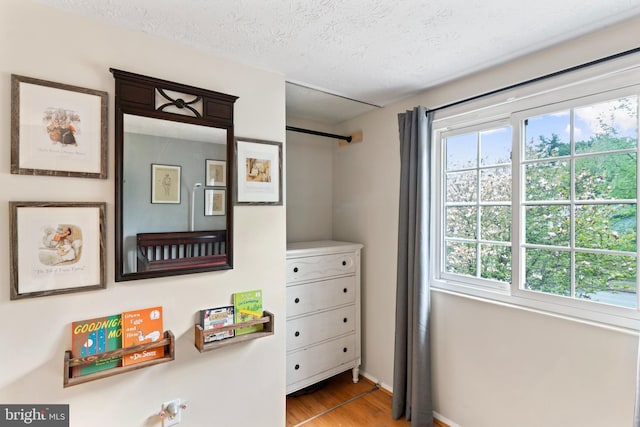 bedroom featuring baseboards, multiple windows, a textured ceiling, and light wood-style floors