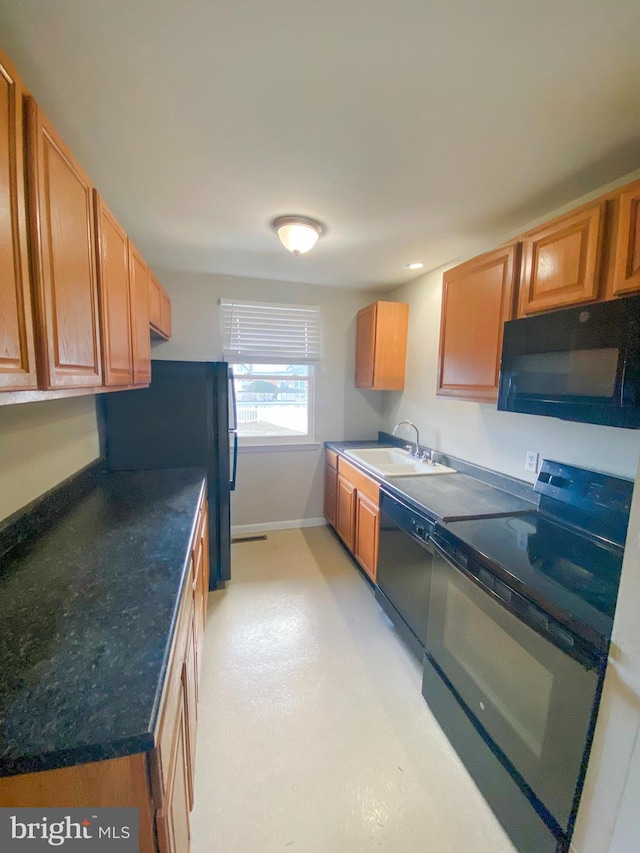 kitchen with dark countertops, black appliances, baseboards, and a sink