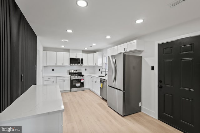 kitchen with visible vents, a sink, appliances with stainless steel finishes, light wood finished floors, and light stone countertops