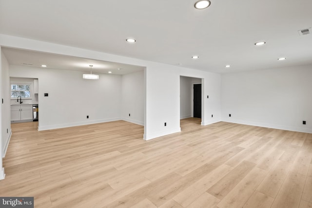 basement featuring visible vents, baseboards, recessed lighting, light wood-style flooring, and a sink