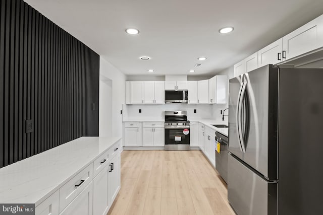 kitchen featuring light wood-style flooring, a sink, appliances with stainless steel finishes, white cabinets, and light stone countertops