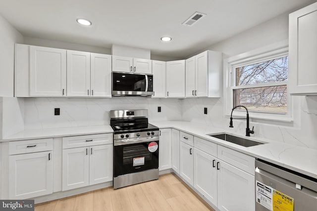 kitchen with visible vents, light wood-style flooring, a sink, white cabinetry, and appliances with stainless steel finishes