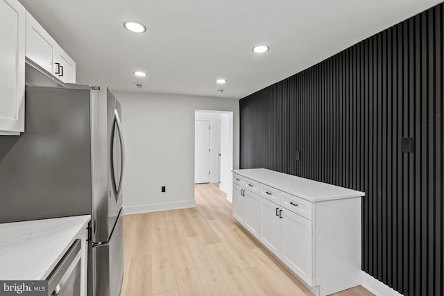 kitchen featuring light stone counters, light wood finished floors, recessed lighting, freestanding refrigerator, and white cabinets