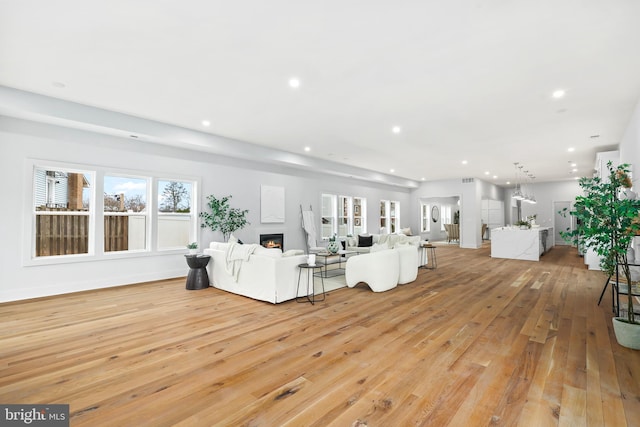 unfurnished living room featuring recessed lighting, a warm lit fireplace, light wood-style flooring, and baseboards