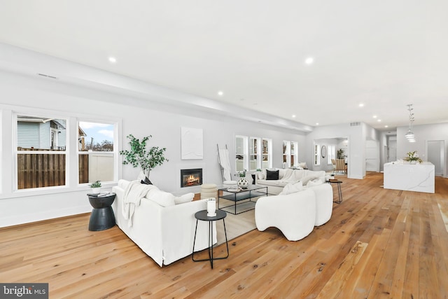 living area with light wood-style floors, recessed lighting, a glass covered fireplace, and visible vents