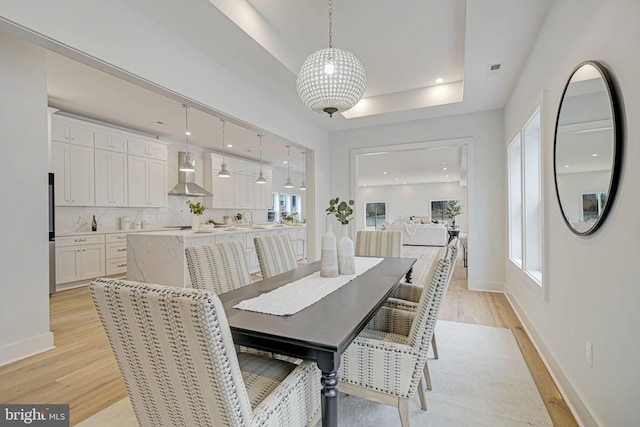 dining space with a tray ceiling, light wood-style flooring, and baseboards