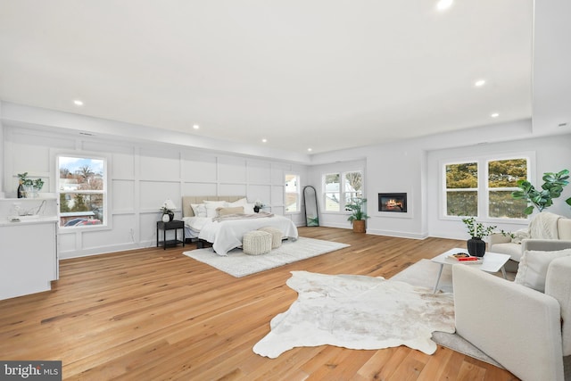 bedroom featuring light wood-type flooring, a glass covered fireplace, and recessed lighting