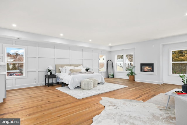 bedroom with light wood-style floors, multiple windows, a decorative wall, and a glass covered fireplace