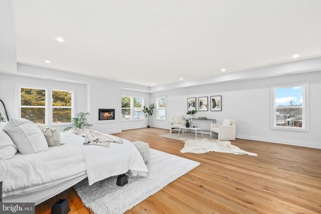 bedroom featuring light wood finished floors, recessed lighting, baseboards, and a glass covered fireplace