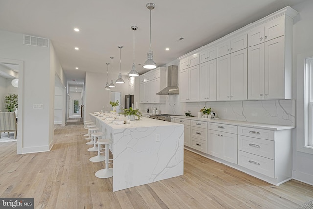 kitchen featuring tasteful backsplash, visible vents, white cabinets, light wood-type flooring, and wall chimney range hood