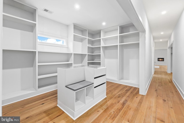 walk in closet featuring a lit fireplace, light wood-type flooring, and visible vents