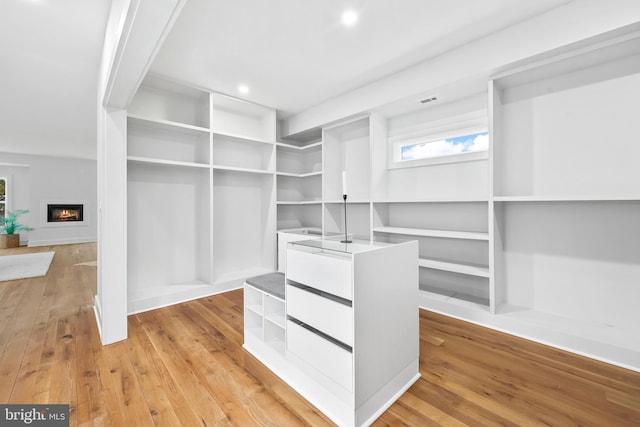 spacious closet featuring visible vents, a glass covered fireplace, and light wood-style flooring