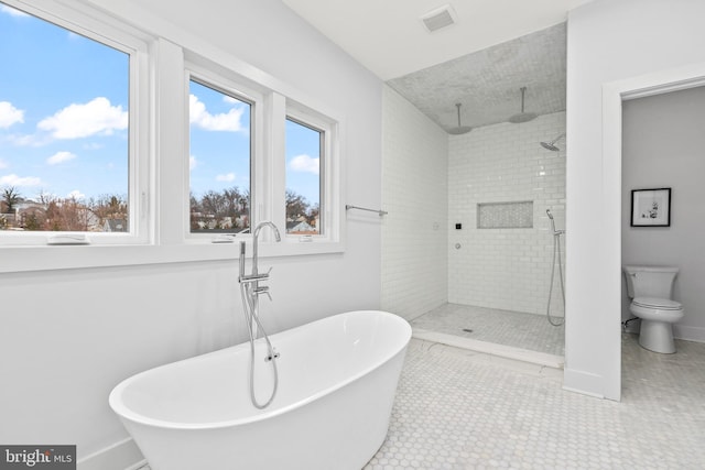 bathroom with toilet, visible vents, baseboards, a freestanding bath, and tiled shower