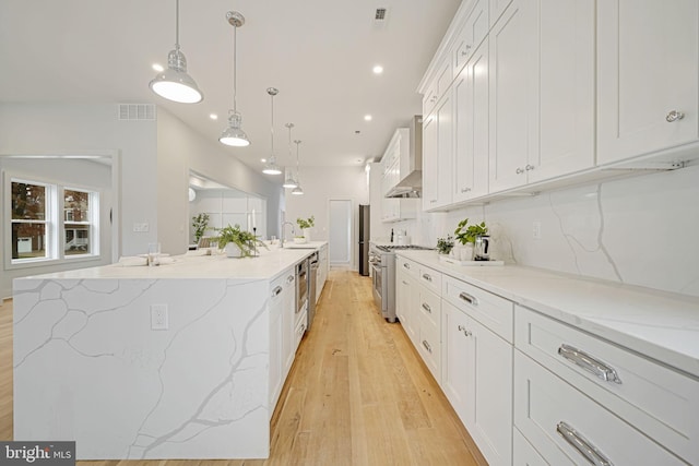 kitchen featuring visible vents, a large island, stainless steel stove, wall chimney range hood, and white cabinetry