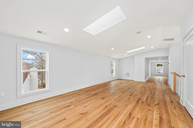 unfurnished living room with vaulted ceiling with skylight, baseboards, visible vents, and light wood finished floors