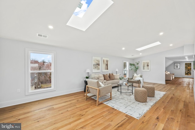 living room with vaulted ceiling with skylight, wood-type flooring, visible vents, and a healthy amount of sunlight