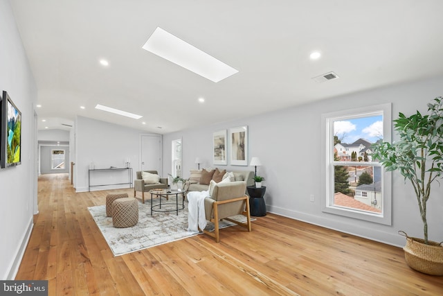 living area featuring light wood finished floors, recessed lighting, visible vents, lofted ceiling with skylight, and baseboards