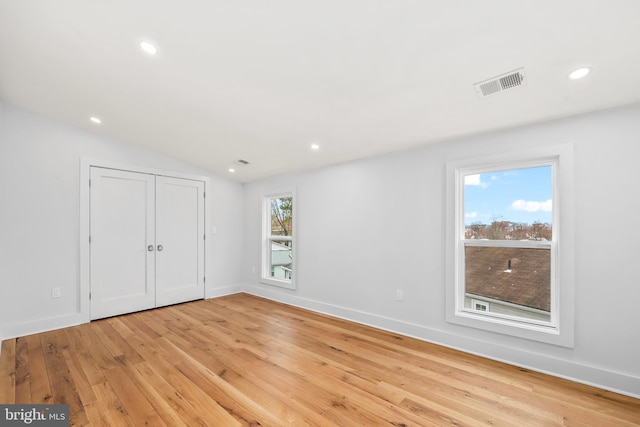 empty room featuring light wood finished floors, recessed lighting, lofted ceiling, visible vents, and baseboards