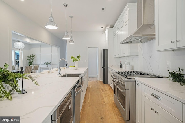 kitchen with backsplash, appliances with stainless steel finishes, white cabinetry, a sink, and wall chimney range hood