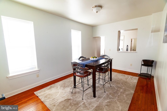 dining room featuring wood-type flooring, a healthy amount of sunlight, and baseboards