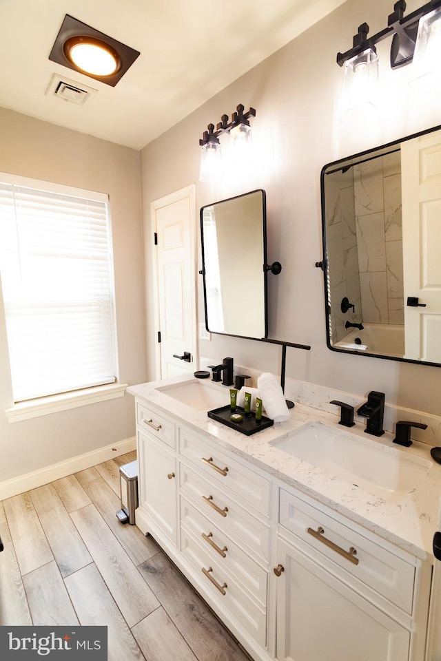 bathroom with double vanity, wood finished floors, a sink, and visible vents