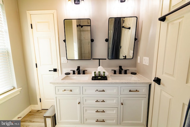 full bath with double vanity, baseboards, a sink, and wood finished floors