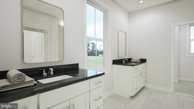 full bathroom featuring a healthy amount of sunlight, two vanities, and a sink