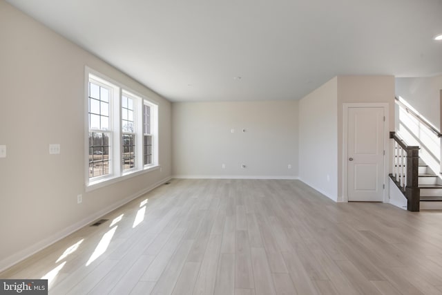 unfurnished living room with light wood-style floors, baseboards, stairs, and visible vents