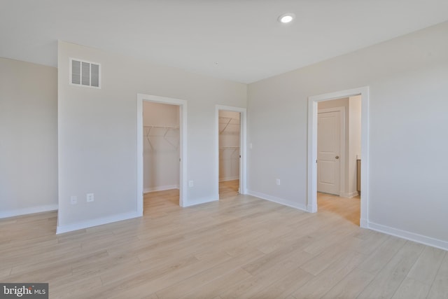 unfurnished bedroom with a walk in closet, recessed lighting, visible vents, light wood-style floors, and baseboards