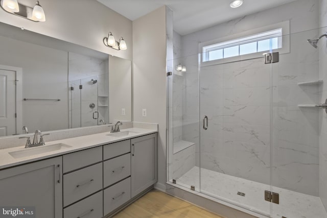 bathroom featuring double vanity, a marble finish shower, a sink, and wood finished floors