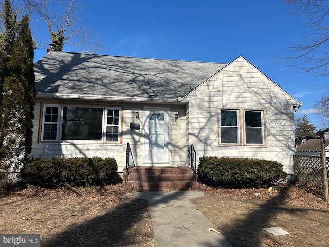 bungalow-style home with a shingled roof and fence